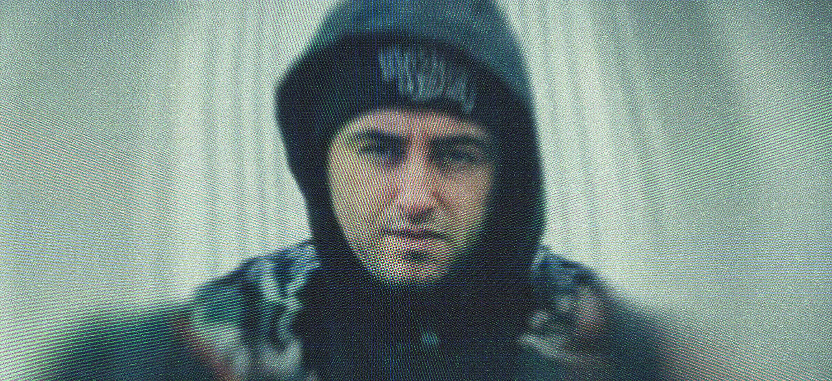 Close-up of Glasgow hip-hop producer Jay-Lee wearing a hoodie, looking intently at the camera against a rippled, grainy backdrop.