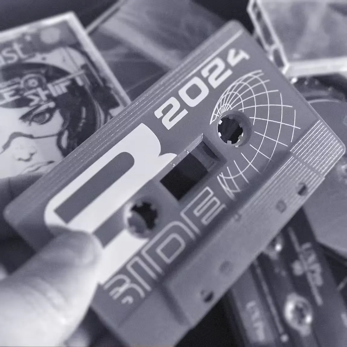 A hand holds a clear plastic cassette tape up to the light, revealing the internal spools and magnetic tape, with a softly lit background suggesting a music studio setting.