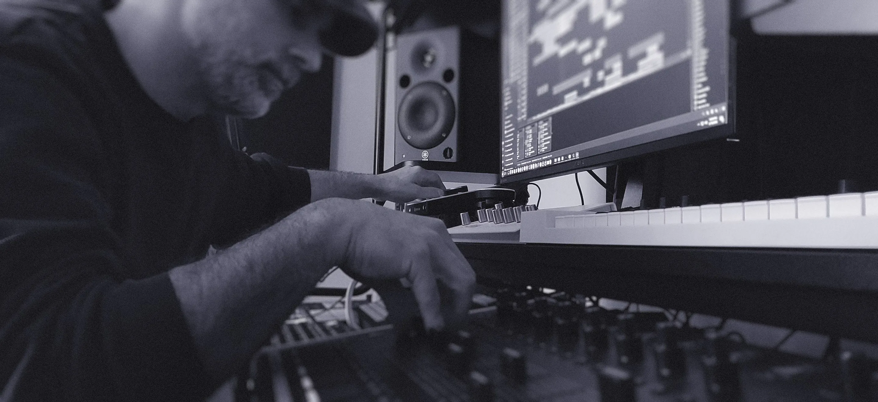 A man works intently on a mixing board, surrounded by recording equipment in a studio setting.
