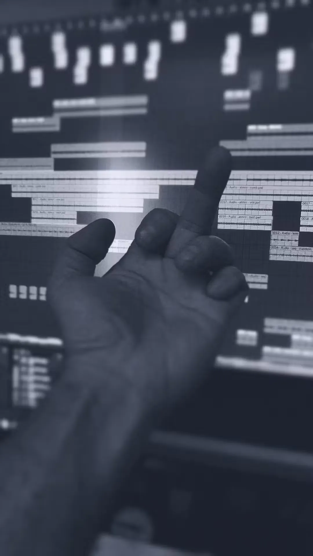 A hand is raised with the middle finger extended, silhouetted against a computer screen displaying an audio editing software interface, conveying frustration.