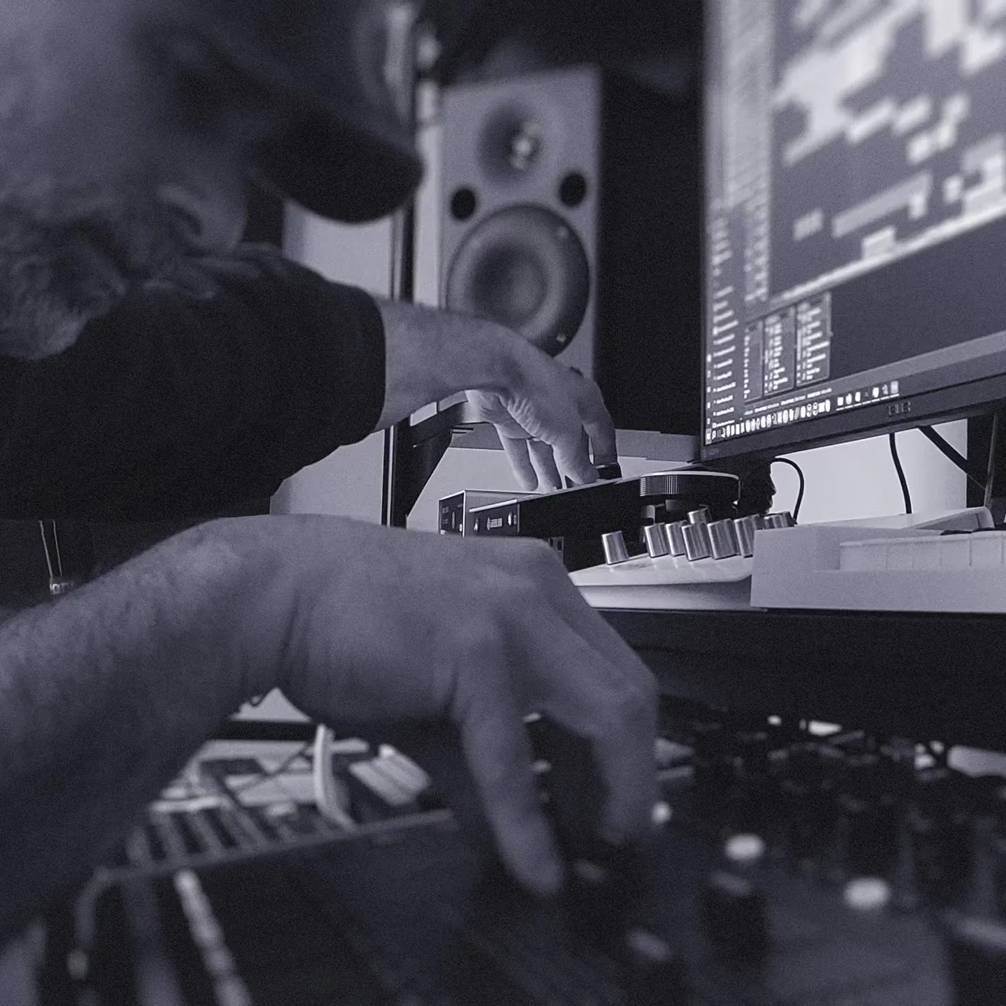 Close-up of music producer adjusting audio mixing controls beside computer running digital audio workstation.