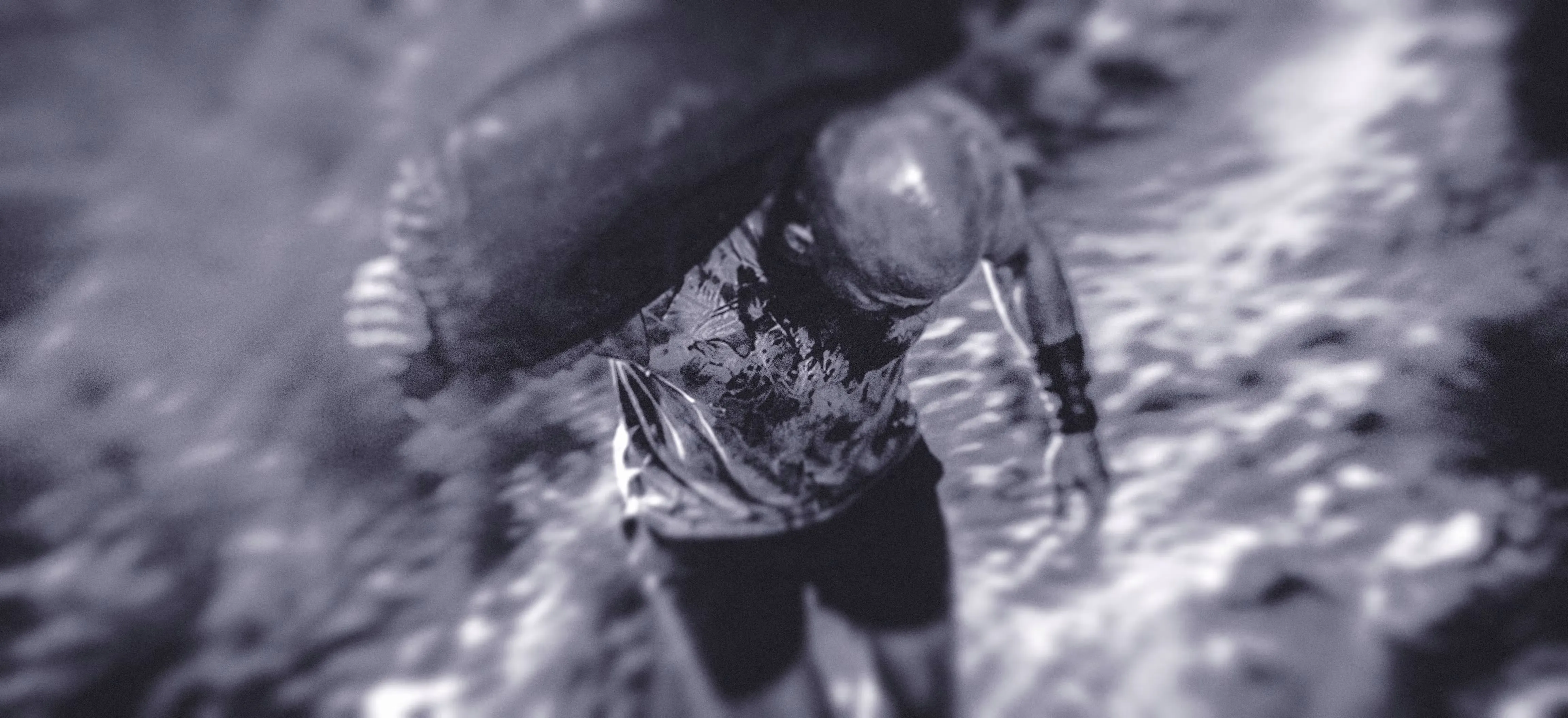 A blurry, monochrome image shows a man running with a sandbag over his shoulder through a trail, viewed from above. The scene conveys a sense of urgency and chaos, with swirling textures.