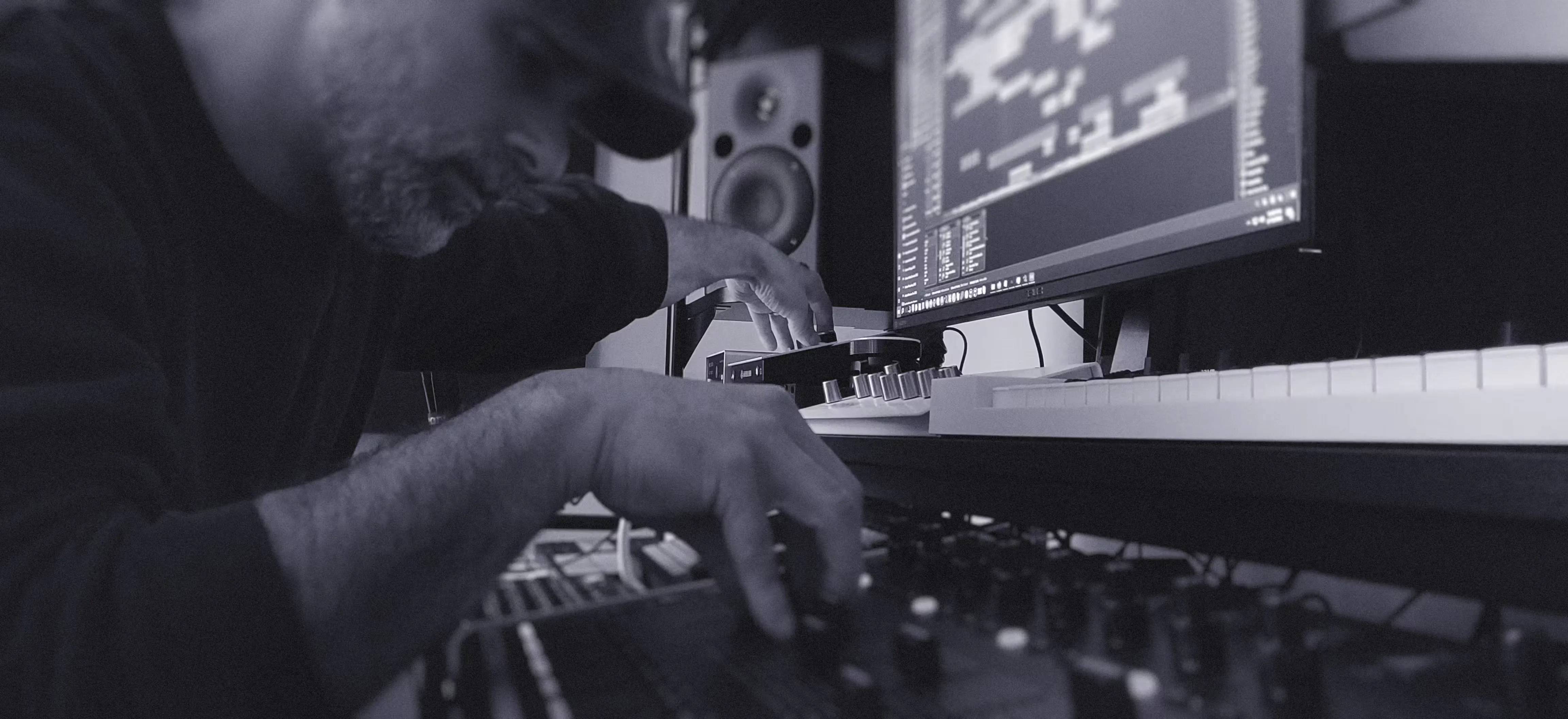 Close-up of music producer adjusting audio mixing controls beside computer running digital audio workstation.