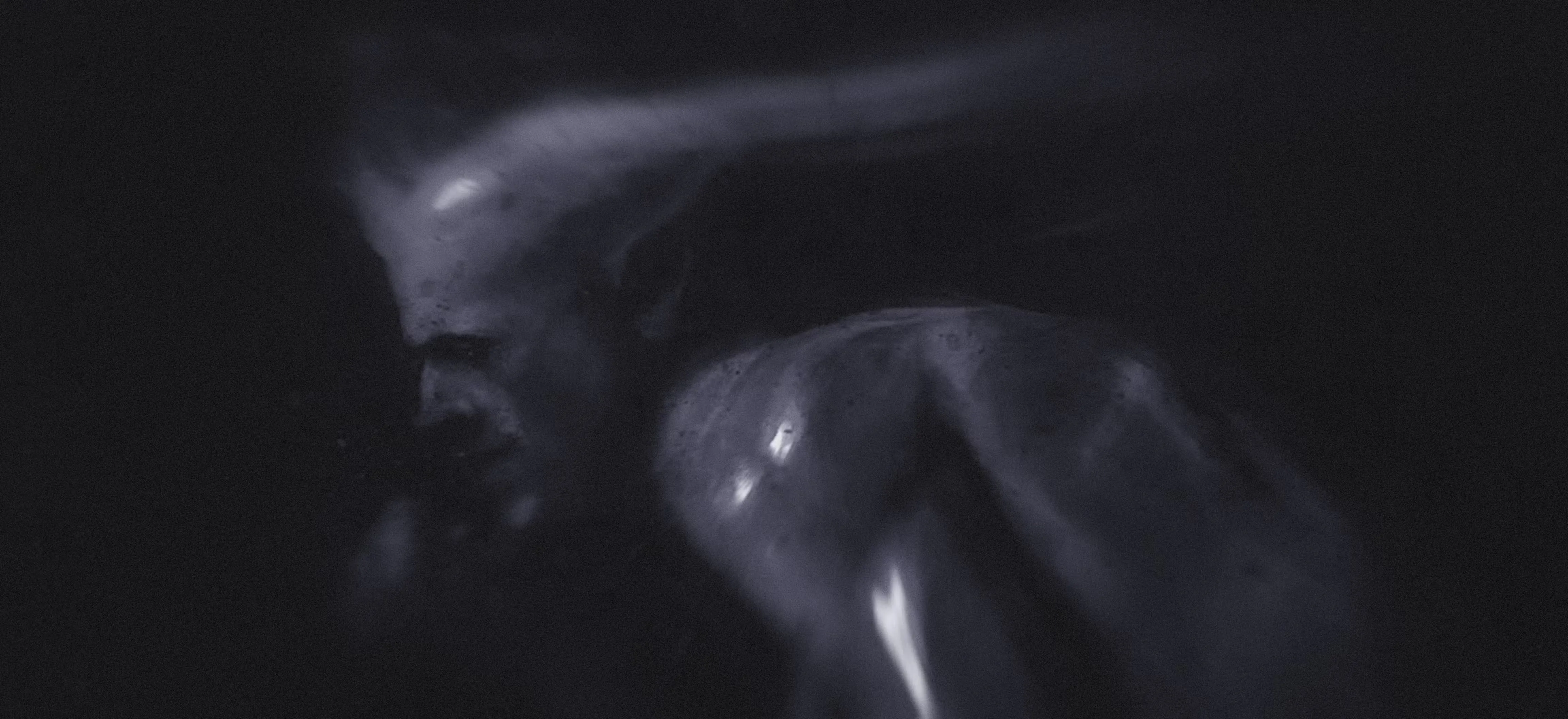 In a dark setting, a devilish man stands with his head down, reflecting a mood of solitude or deep thought.