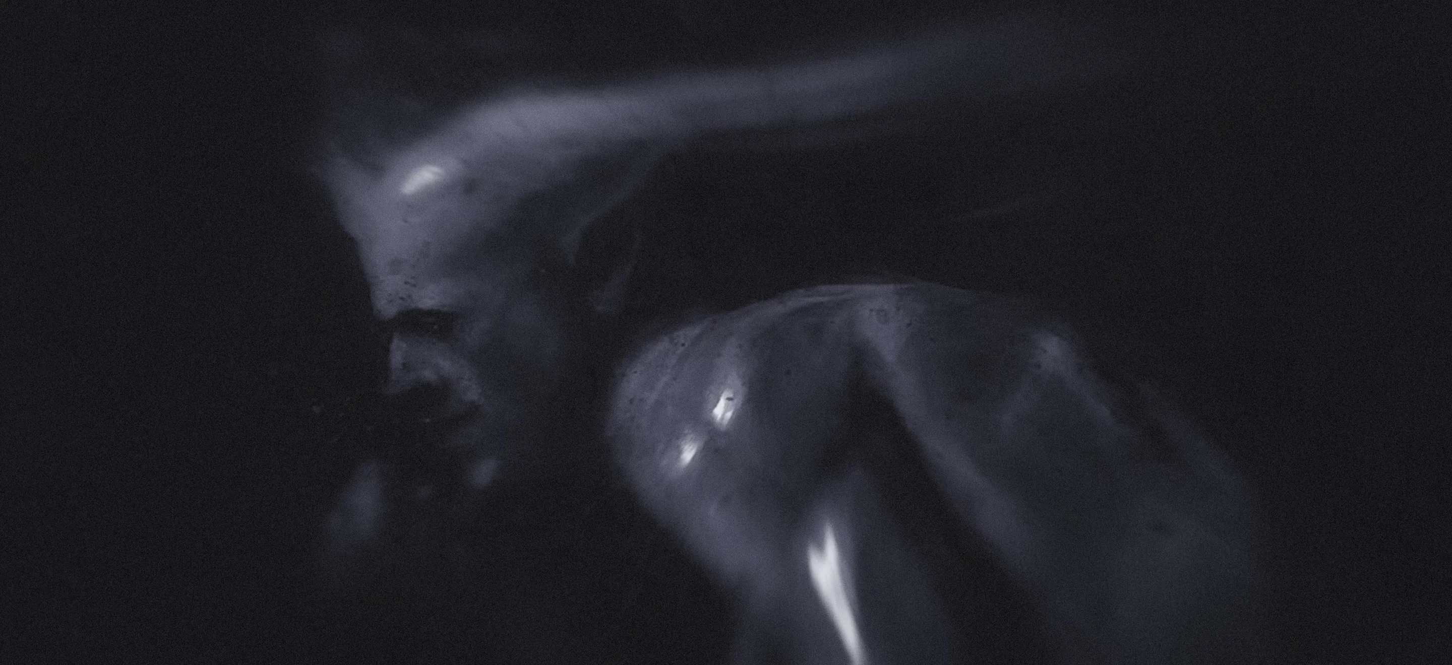 In a dark setting, a devilish man stands with his head down, reflecting a mood of solitude or deep thought.