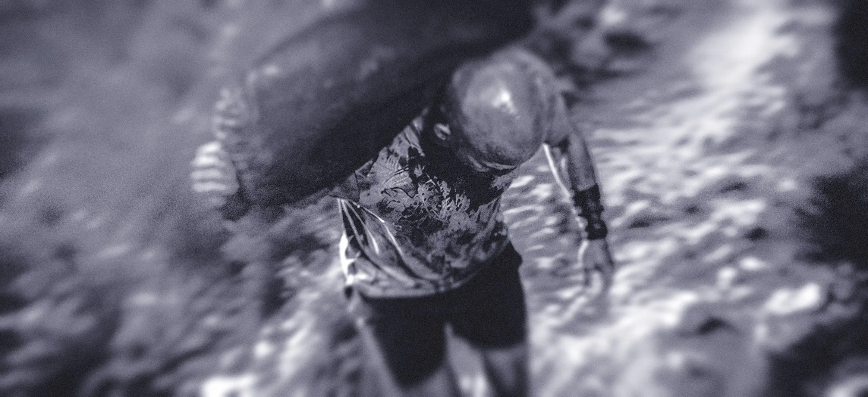 A blurry, monochrome image shows a man running with a sandbag over his shoulder through a trail, viewed from above. The scene conveys a sense of urgency and chaos, with swirling textures.