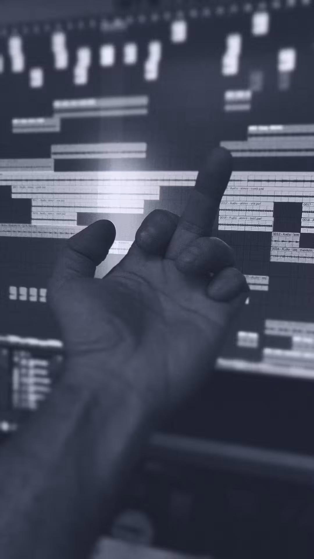 A hand is raised with the middle finger extended, silhouetted against a computer screen displaying an audio editing software interface, conveying frustration.