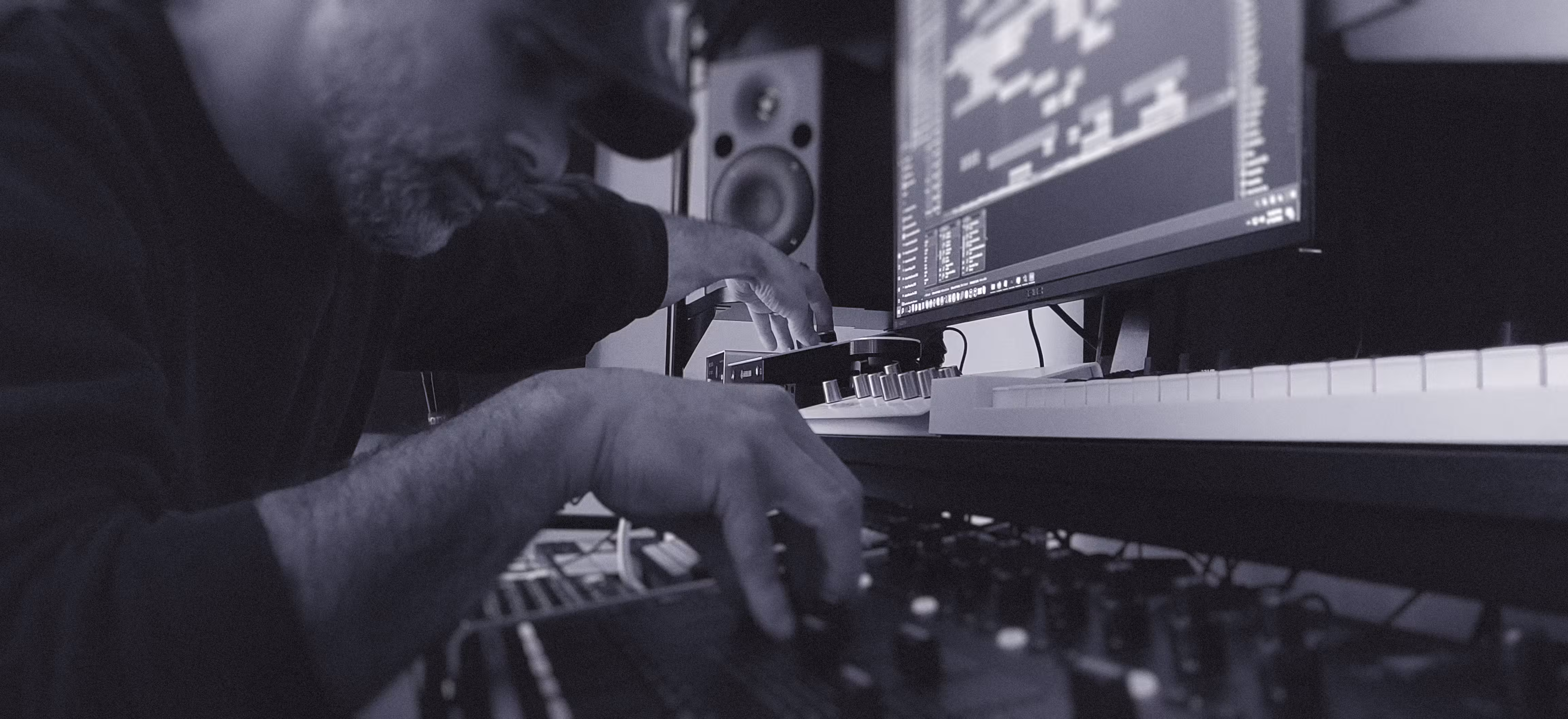 Close-up of music producer adjusting audio mixing controls beside computer running digital audio workstation.