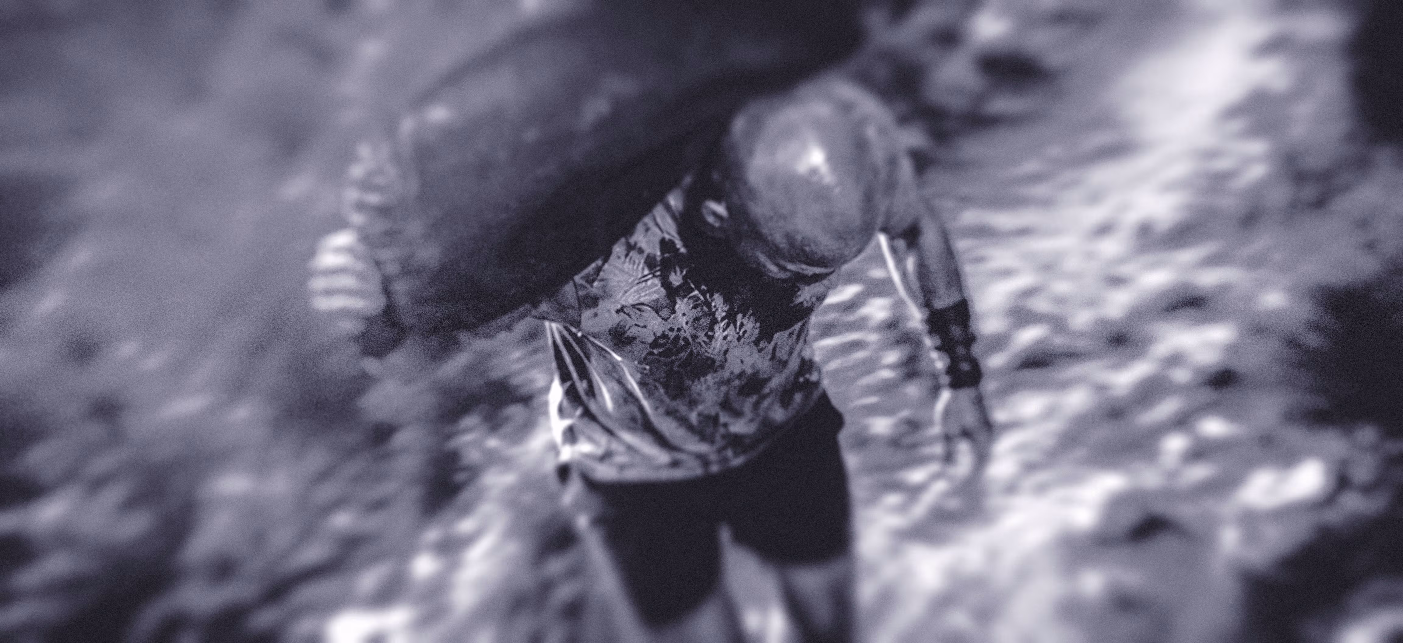A blurry, monochrome image shows a man running with a sandbag over his shoulder through a trail, viewed from above. The scene conveys a sense of urgency and chaos, with swirling textures. The image is used as an analogy in an article for the weight of self-doubt as a music producer.