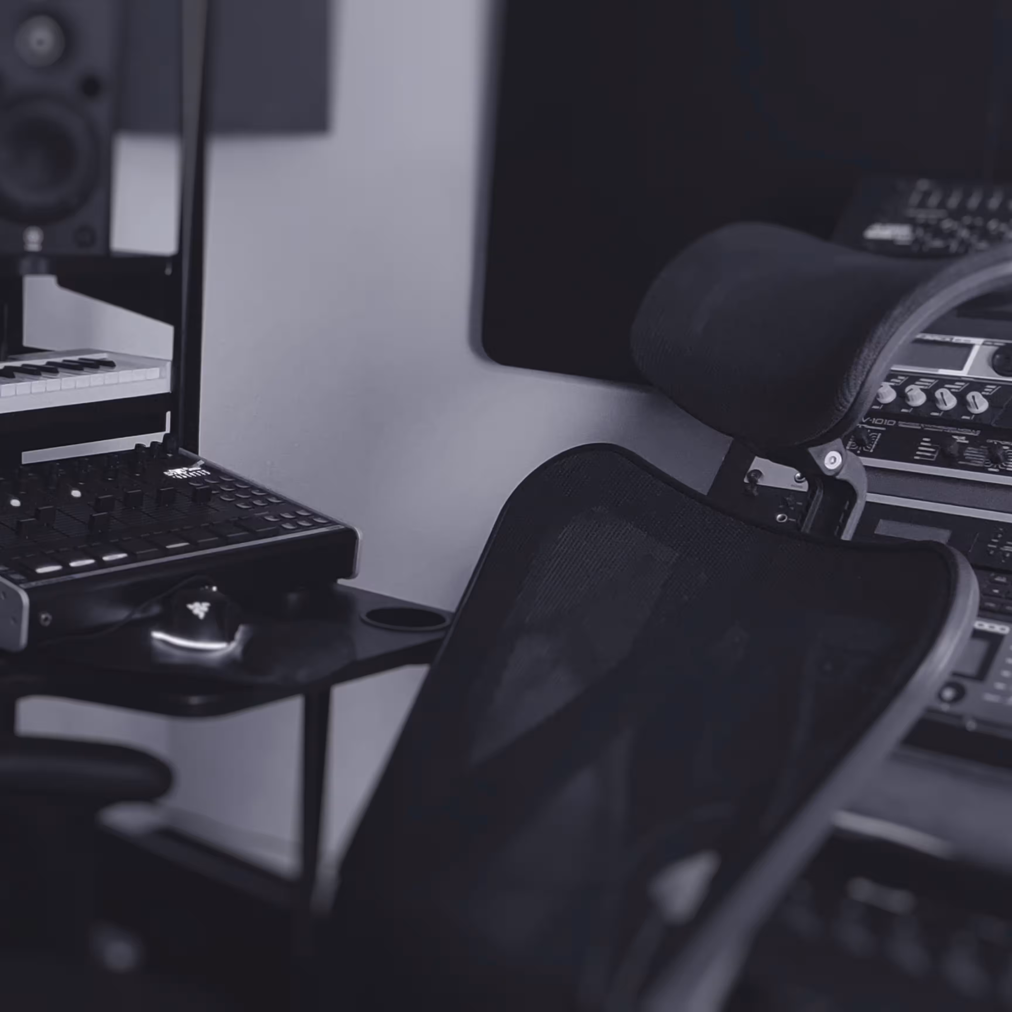 A black mesh office chair is positioned in front of audio equipment, including a mixer, speakers, and rack-mounted gear in a music studio.