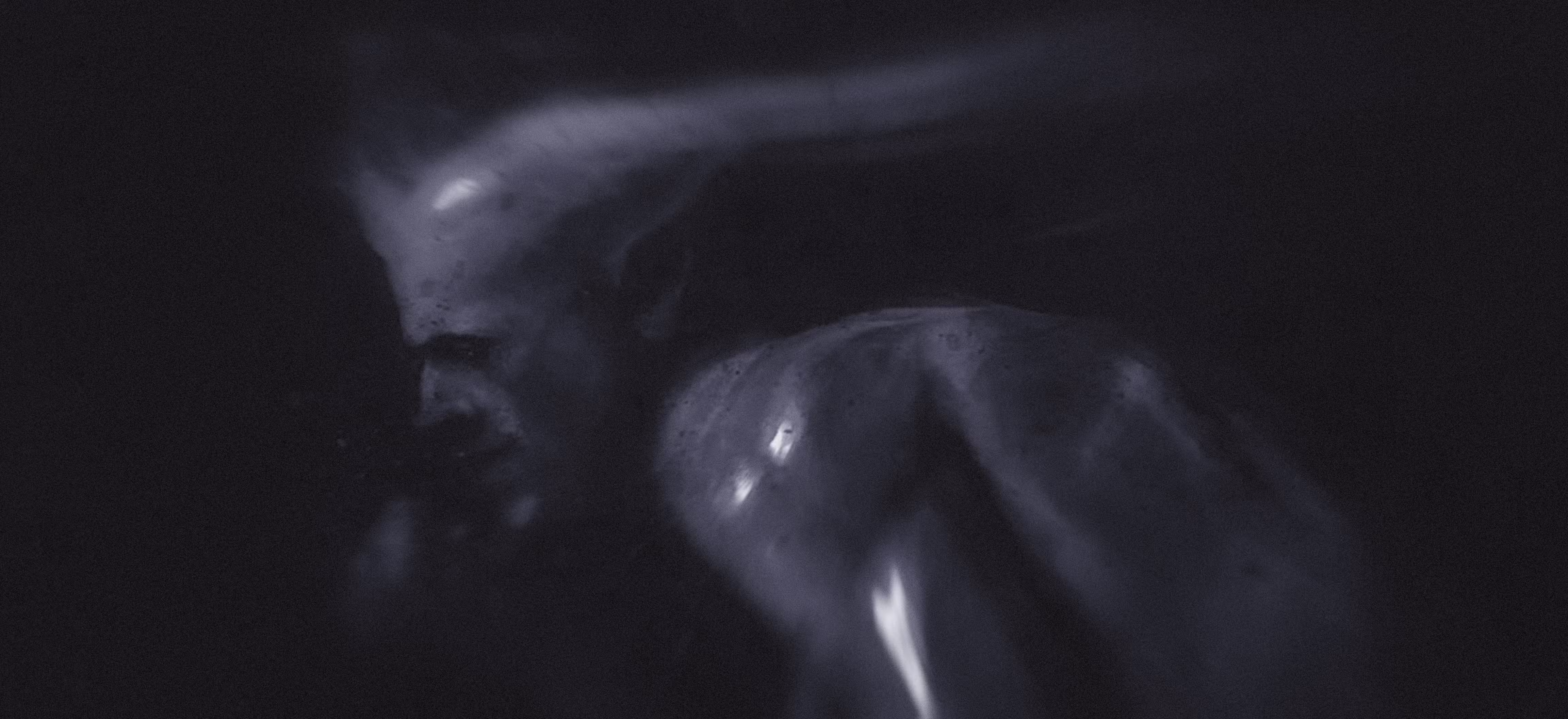 In a dark setting, a devilish man stands with his head down, reflecting a mood of solitude or deep thought.